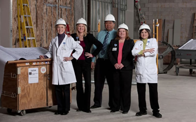 A group of five people on a construction site with hard hats posing for a photograph.