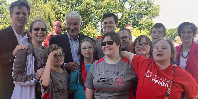 Tom Golisano and Tim Schriver posing with a group of children at a Special Olympics event.