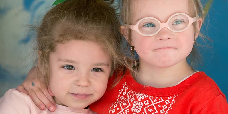 Two young girls, one with her arm around the other wearing glasses