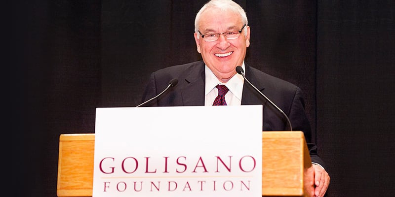 Tom Golisano speaking at a podium with a Golisano Foundation sign on it