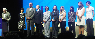 President Clinton speaks with a group on stage at a podium.