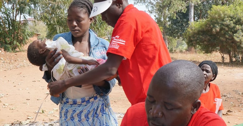 Woman holding child while a volunteer does a health examination.